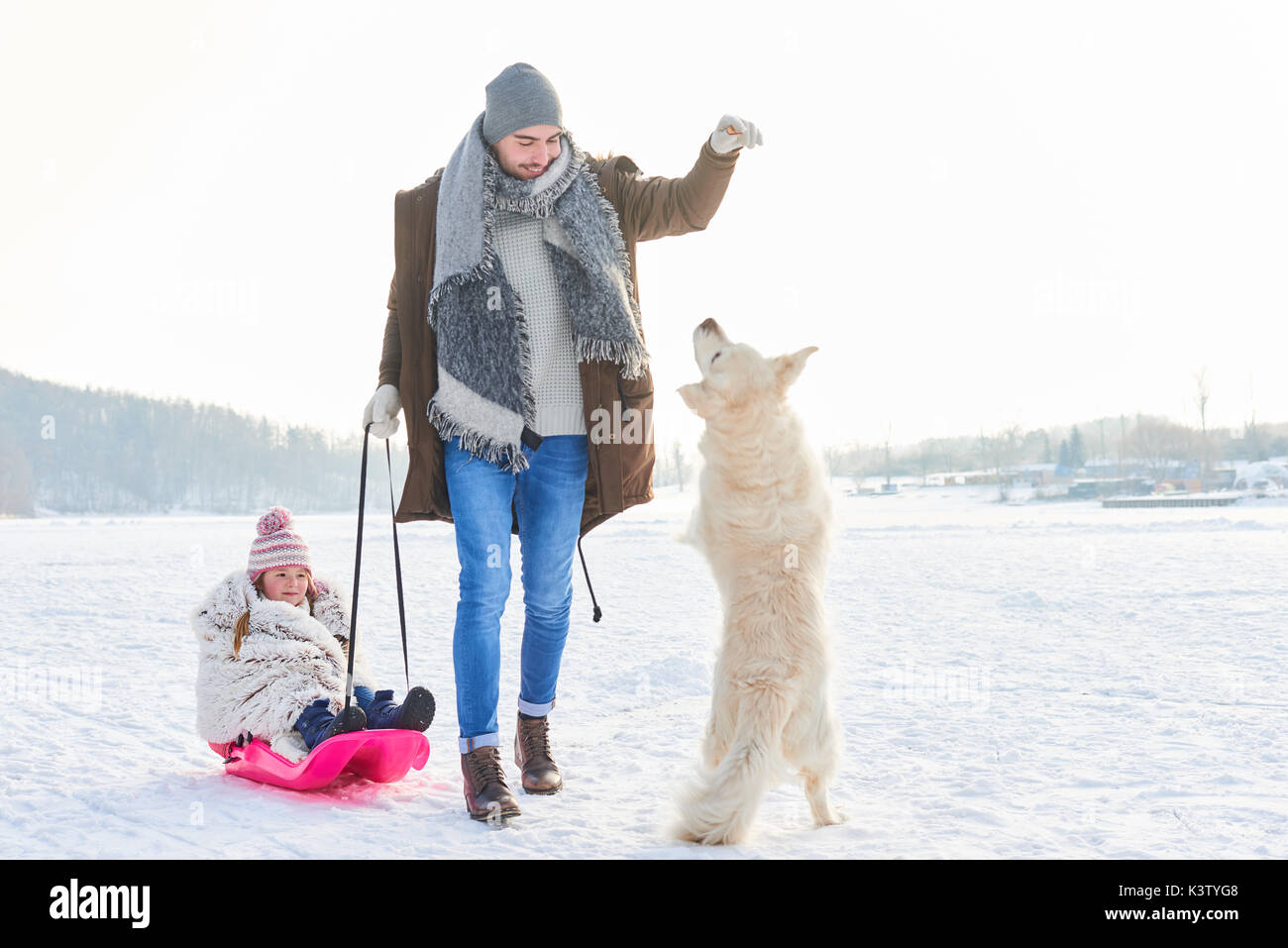 Padre giocando con il cane e la figlia mentre lo slittino in inverno Foto Stock