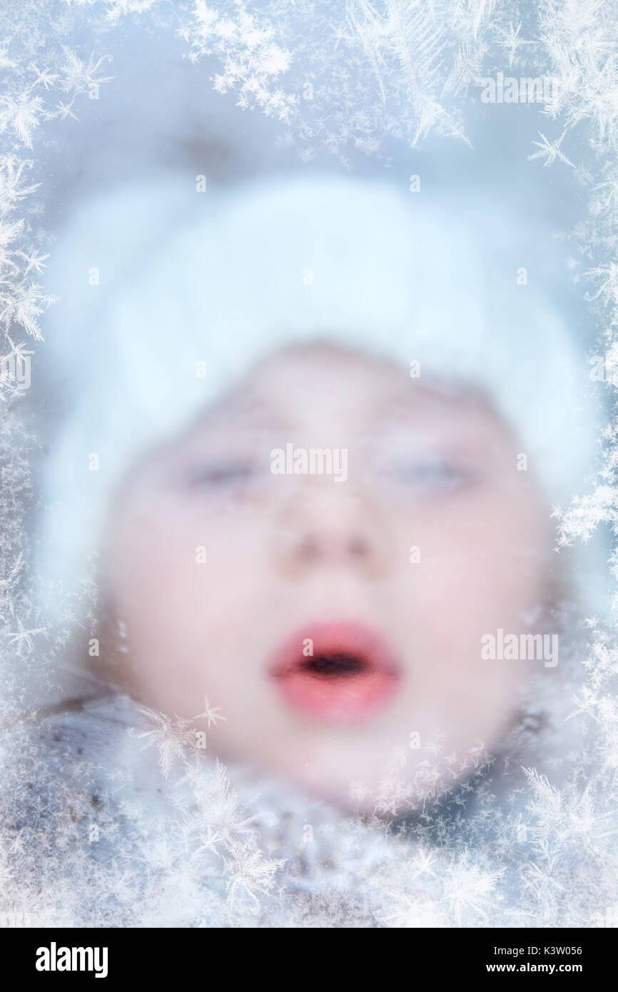 Bambino in inverno soffia sulla finestra ghiacciata con pattern di brina Foto Stock