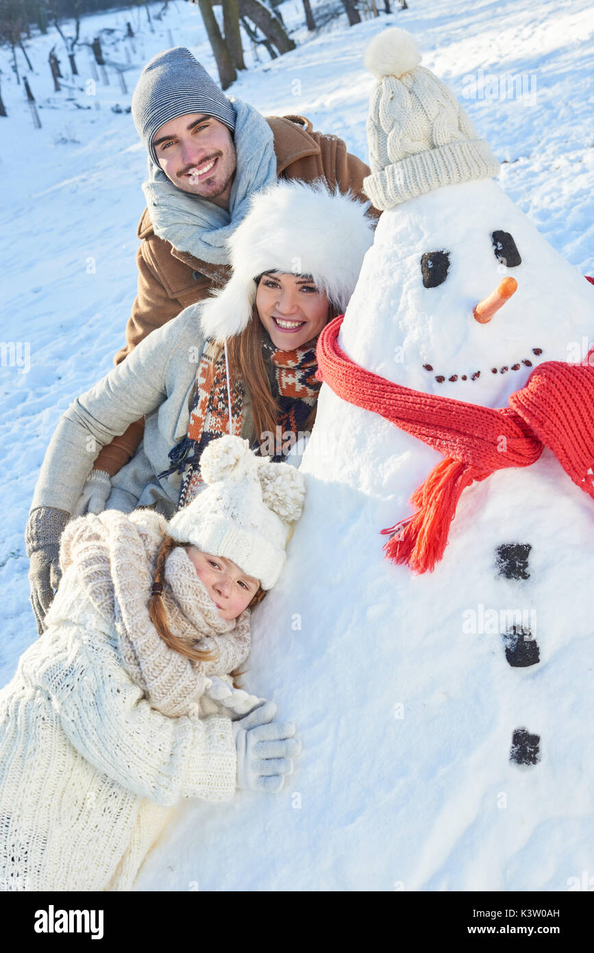 La famiglia felice giocando con il pupazzo di neve in inverno Foto Stock