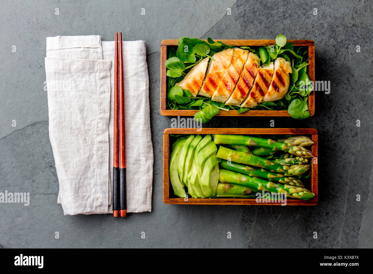 Un sano pranzo in giapponese in legno scatola di Bento. Equilibrato il cibo sano chucken grigliate e avocado con asparagi e insalata verde. Vista superiore, grigio ardesia bac Foto Stock