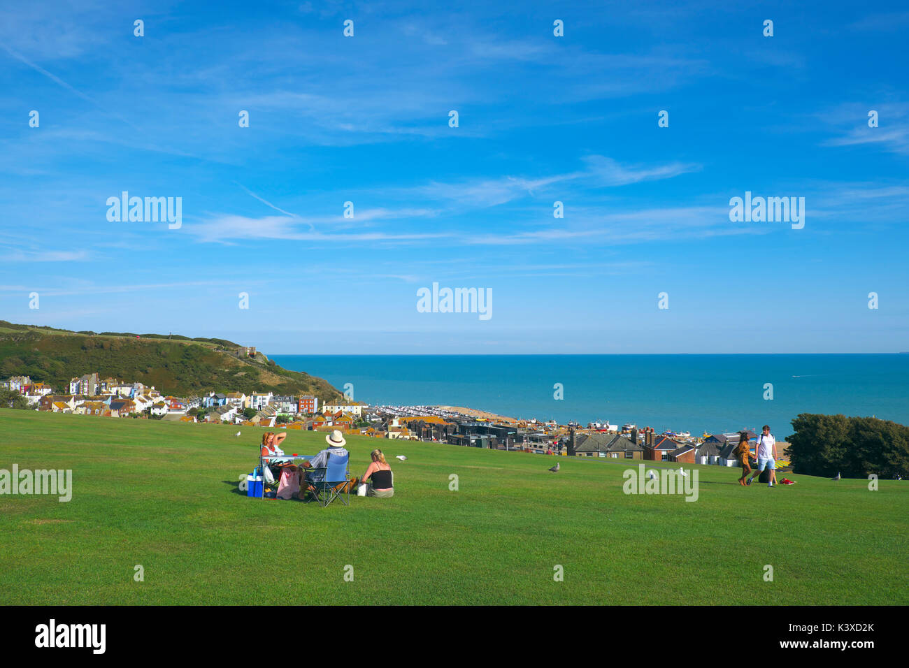 Hastings vista sul West Hill alla vecchia città annidata nella valle sottostante; con persone aventi un picnic sull'erba. East Sussex, Regno Unito, GB Foto Stock