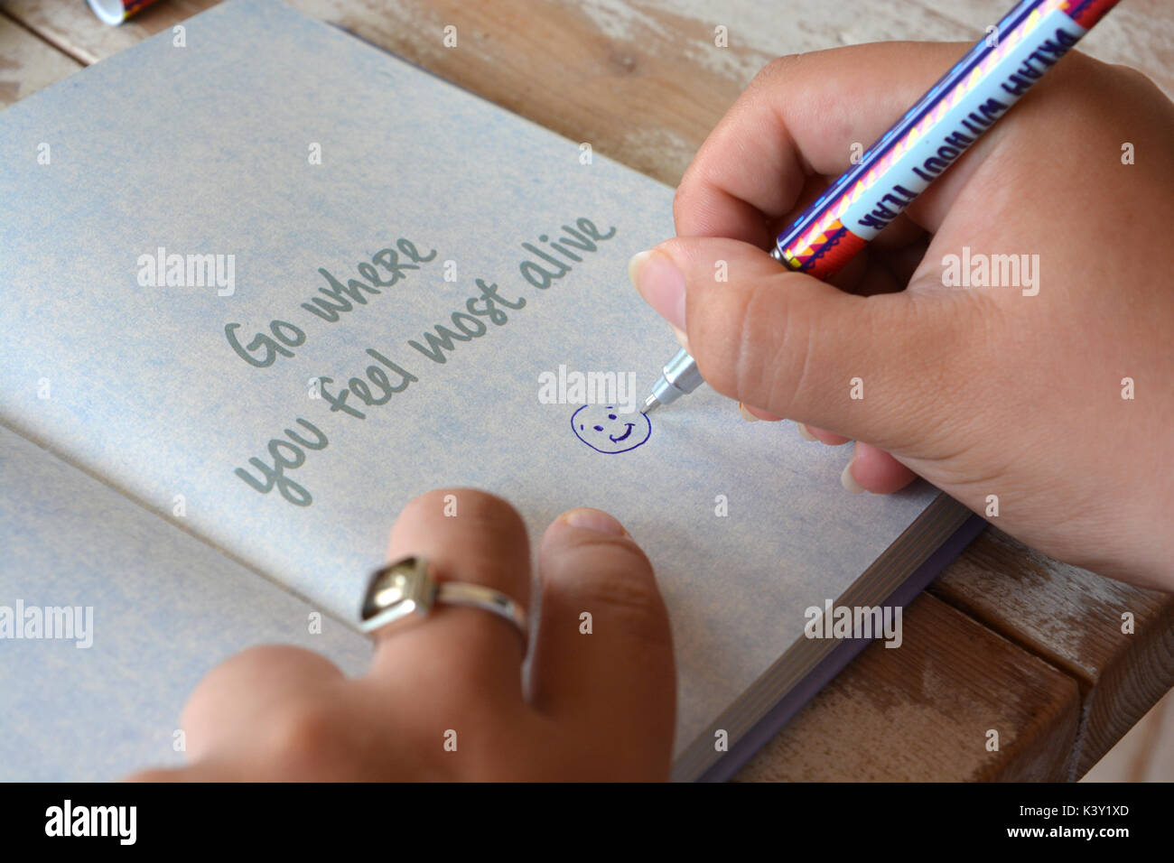 La donna il disegno di una faccina sorridente in un giornale aperto a una pagina con il mantra andare dove ti senti più vivo Foto Stock