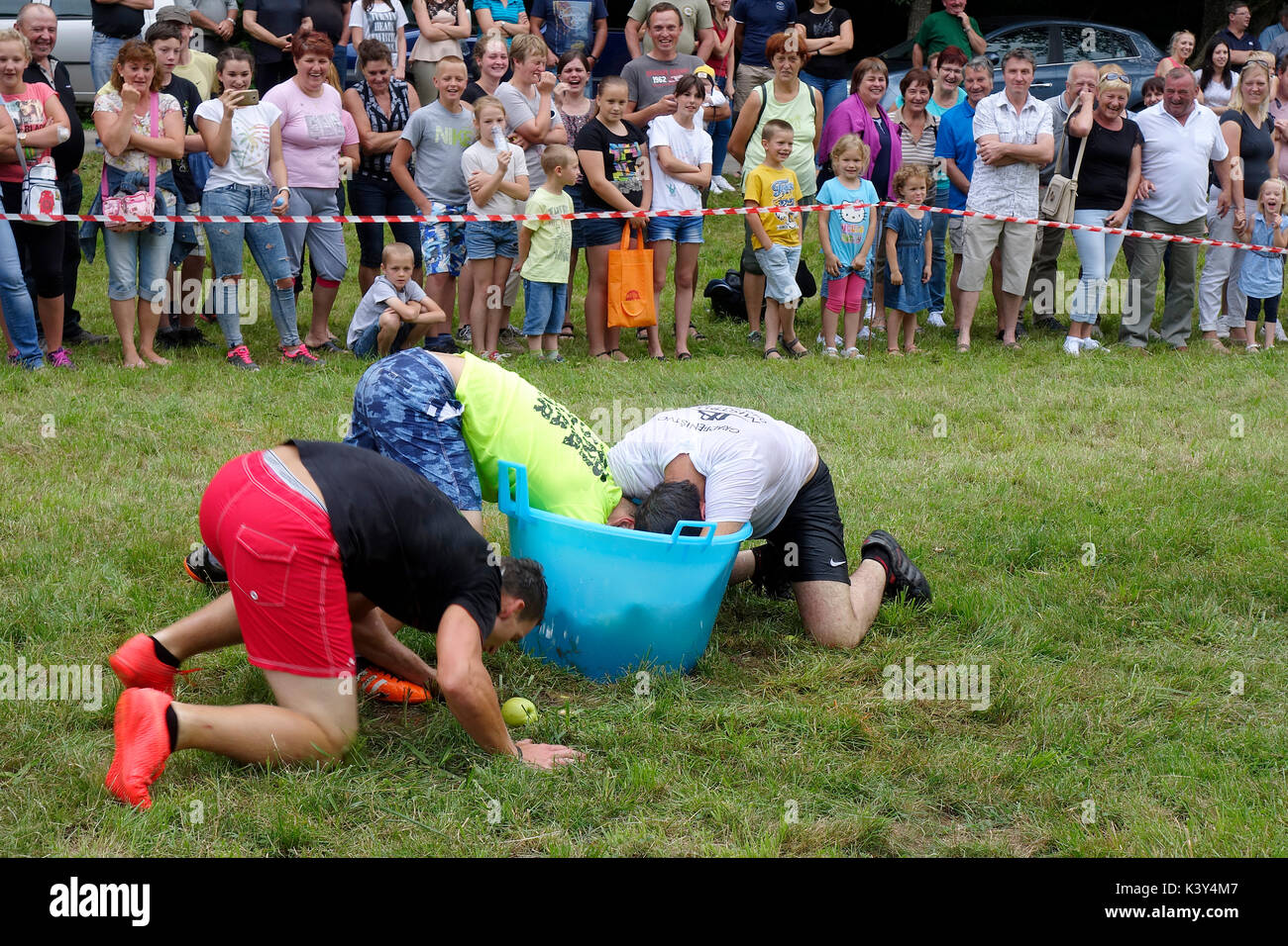 Cheers pubblico mentre i giovani uomini competere in morso e recuperare le mele da acqua depositata in plastica canna a metà dell'agricoltore giochi al villaggio in fiera Tržišče. Dolenjsk Foto Stock