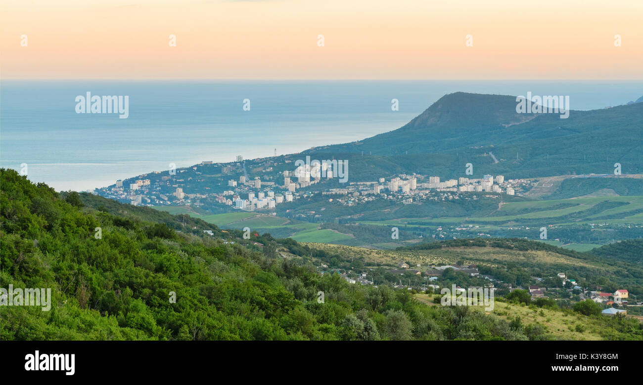 Resort costiero città tra le montagne e colline vicino al mare all'alba. La penisola di Crimea, Alushta Foto Stock