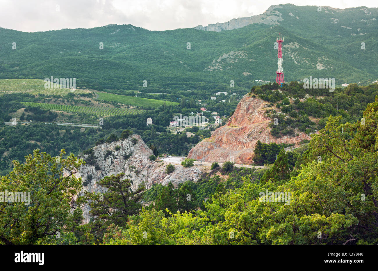 La strada attraverso la roccia con una torre cellulare sulla parte superiore su uno sfondo di colline boscose. Foto Stock