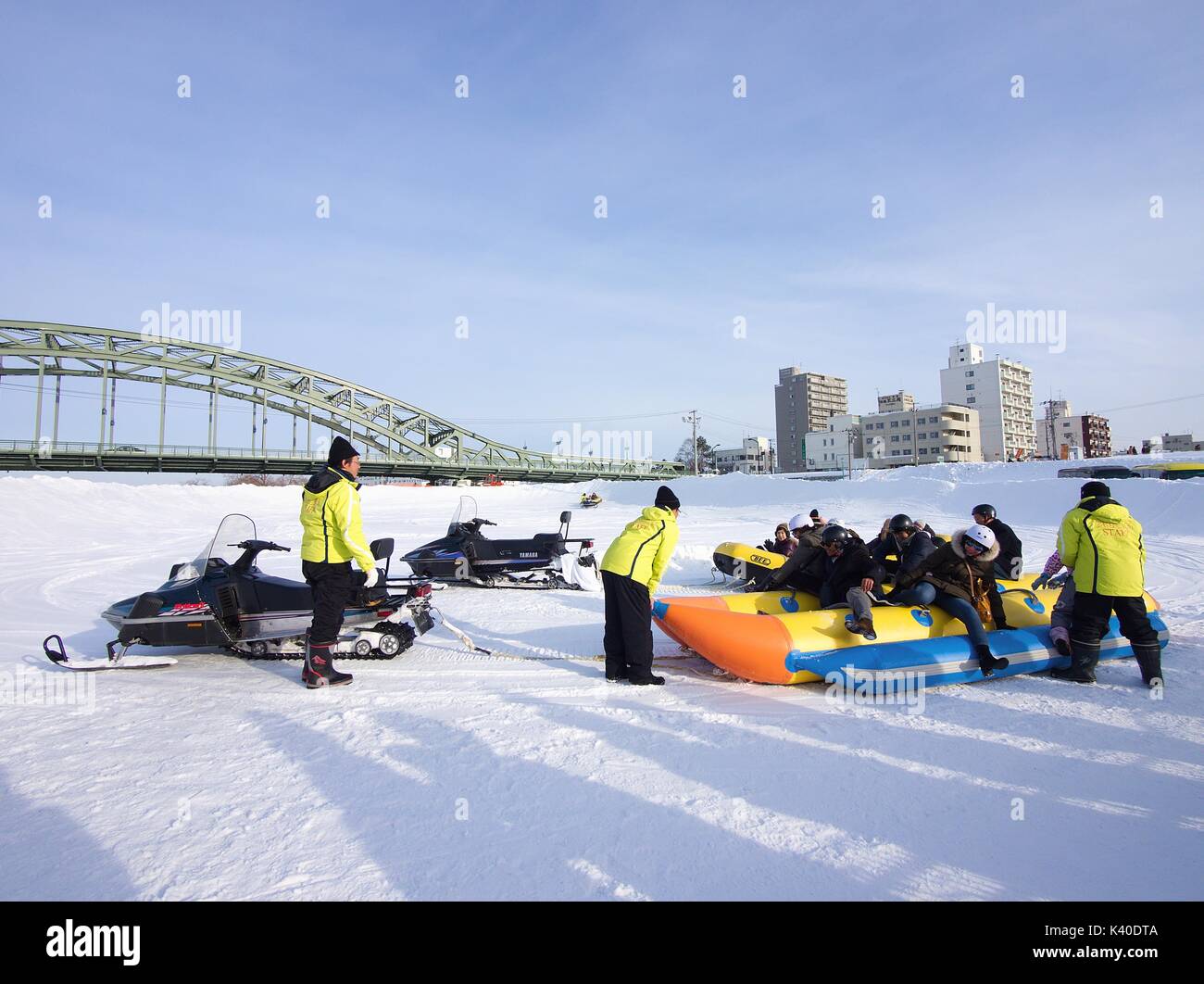 I visitatori si divertono con banana boat sul ghiaccio tirato dalla neve mobile all'Asahikawa Winter Festival, Hokkaido, Giappone Foto Stock
