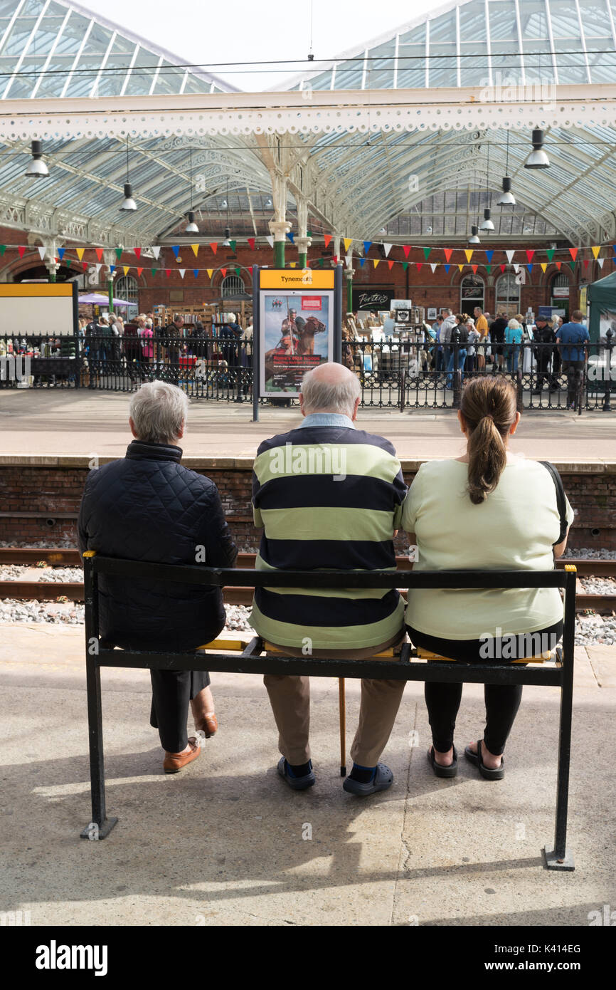 Tre persone sedute, in attesa di un treno della metropolitana sulla stazione di Tynemouth, North East England, Regno Unito Foto Stock