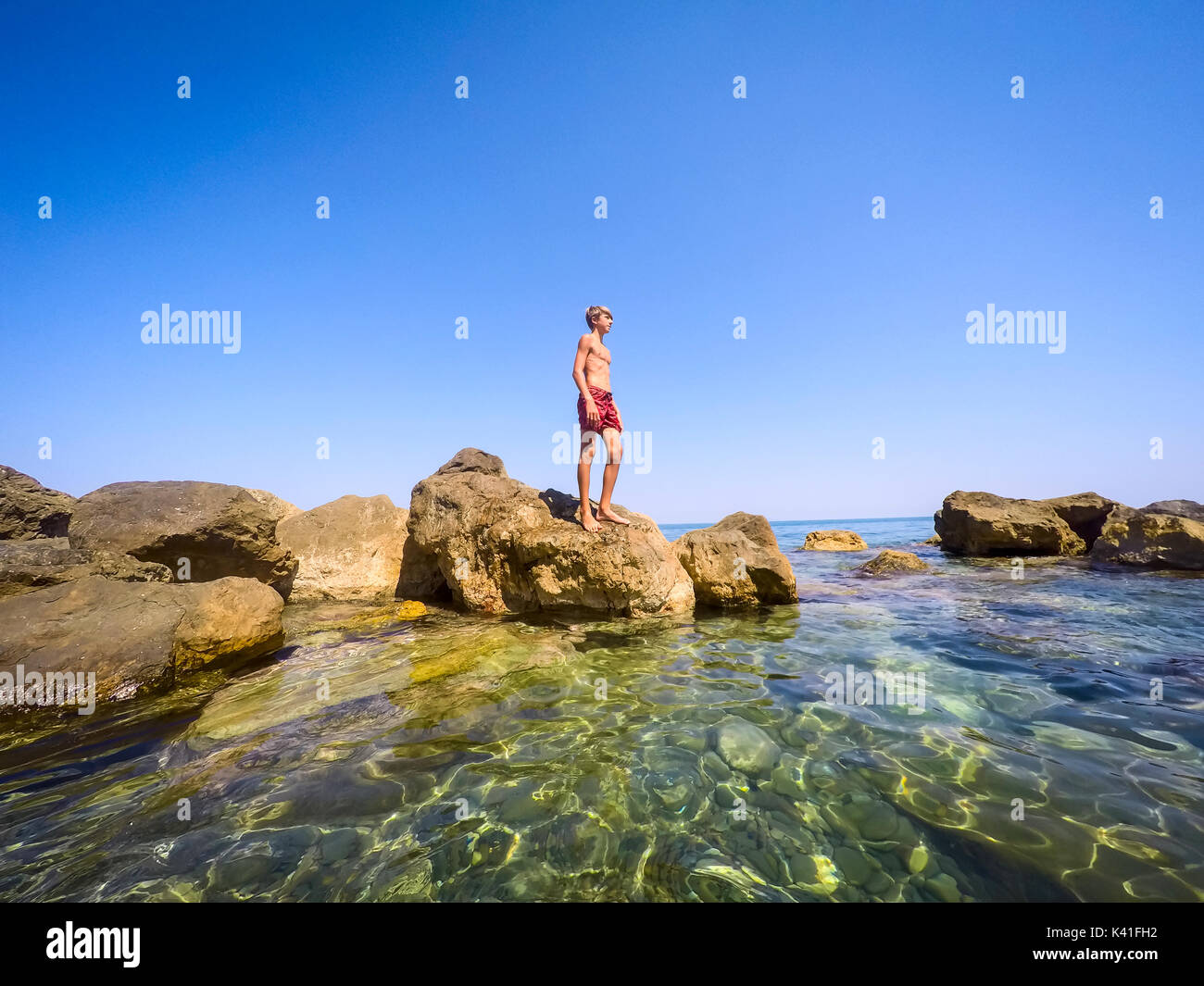 Adolescente in piedi sulle rocce al mare - estate - Sicilia mare mediterraneo Foto Stock