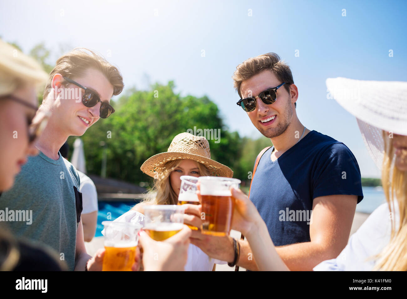 Una foto di gruppo di amici seduti sul molo. Si sta sollevando un brindisi con la birra. Foto Stock