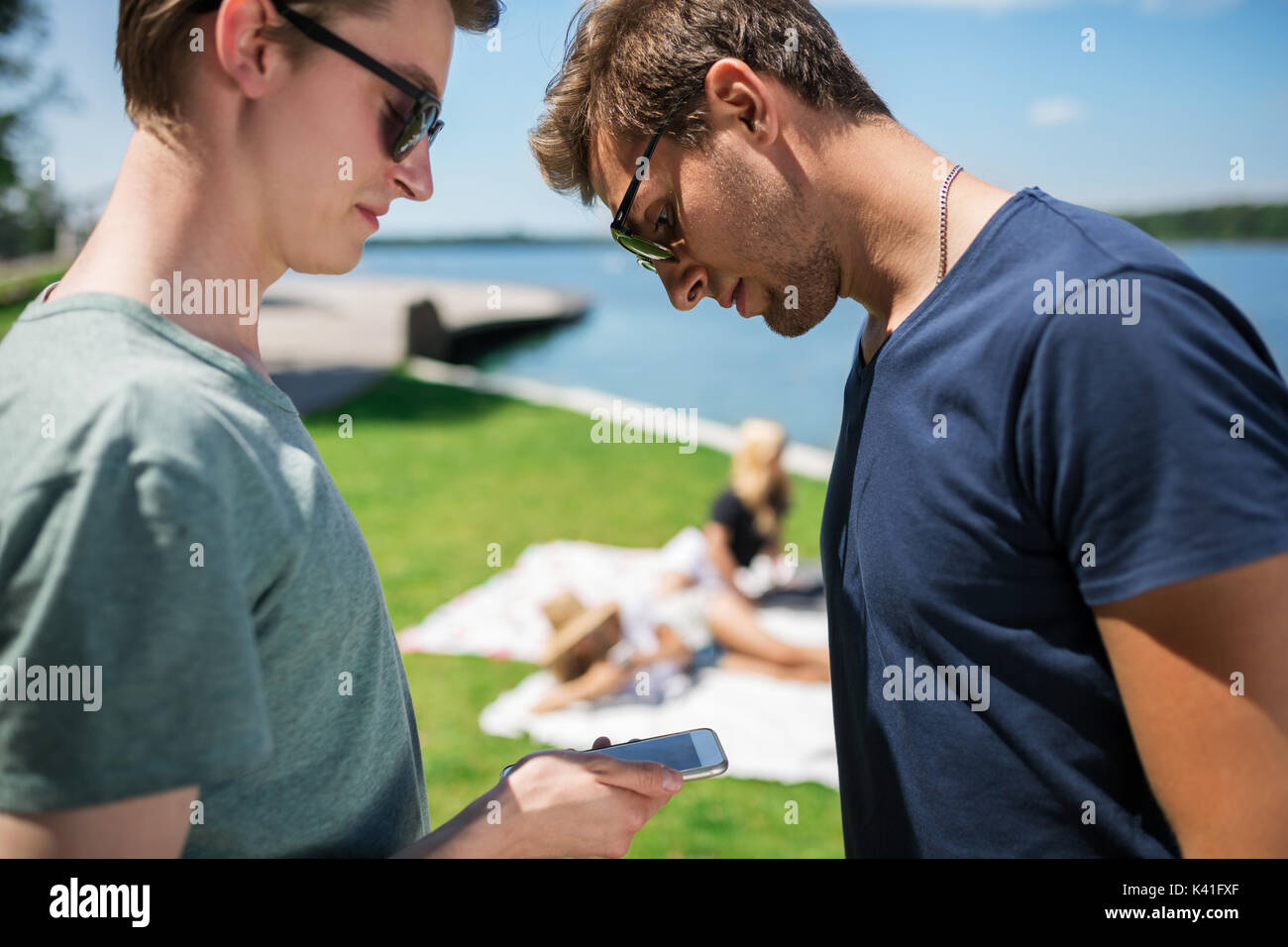 Una foto di due amici che trascorrono il loro tempo al lago. Essi stanno guardando qualcosa sul telefono cellulare. Foto Stock