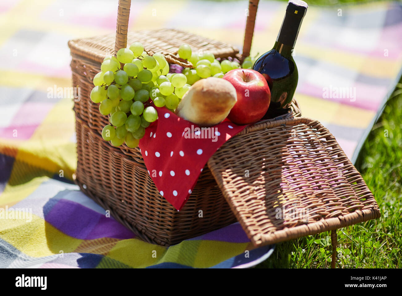 La foto di un cestino pic-nic in piedi sulla coperta. È riempito con frutta, pane e vino. Foto Stock