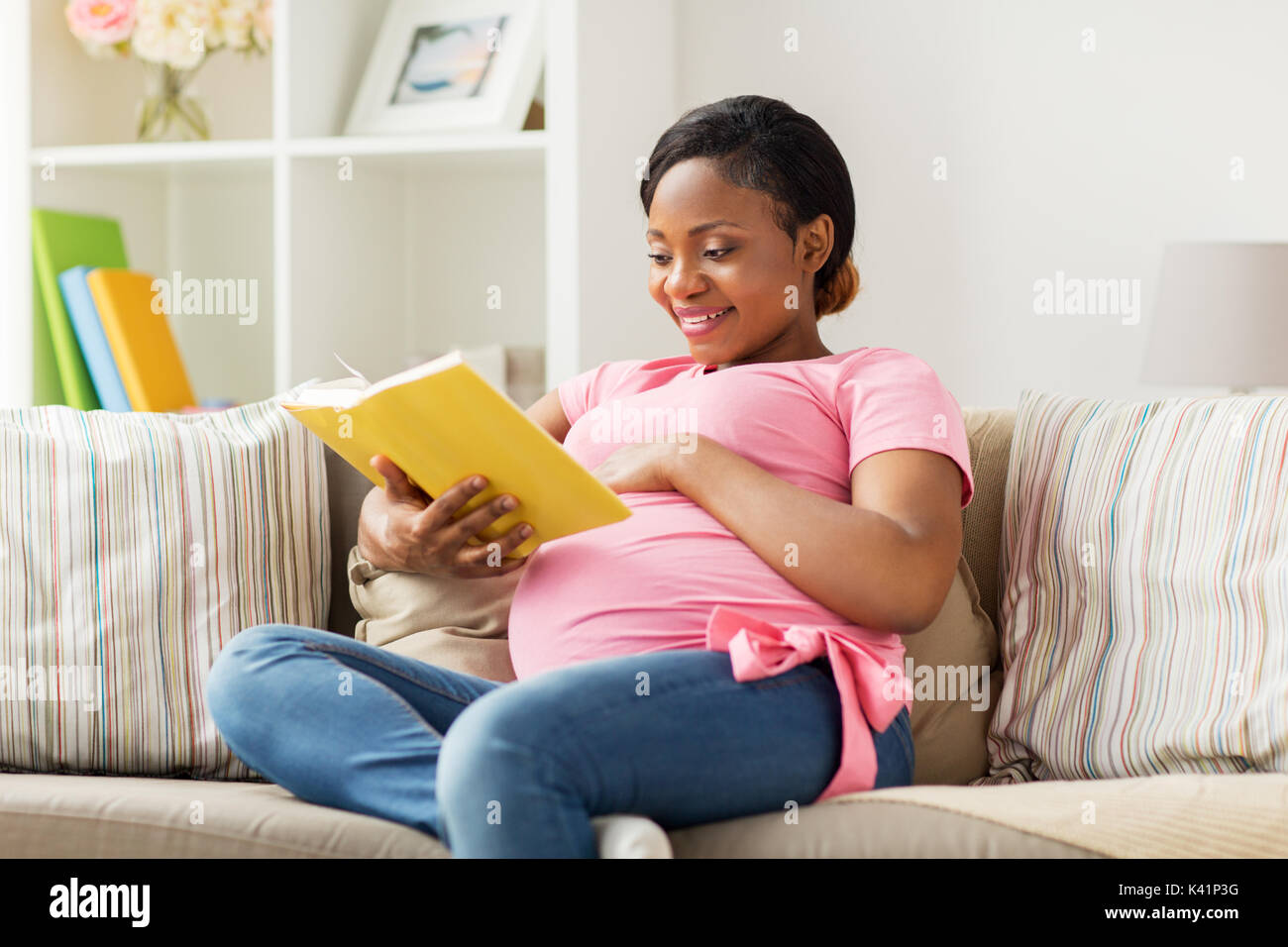 Felice donna africana incinta libro di lettura a casa Foto Stock