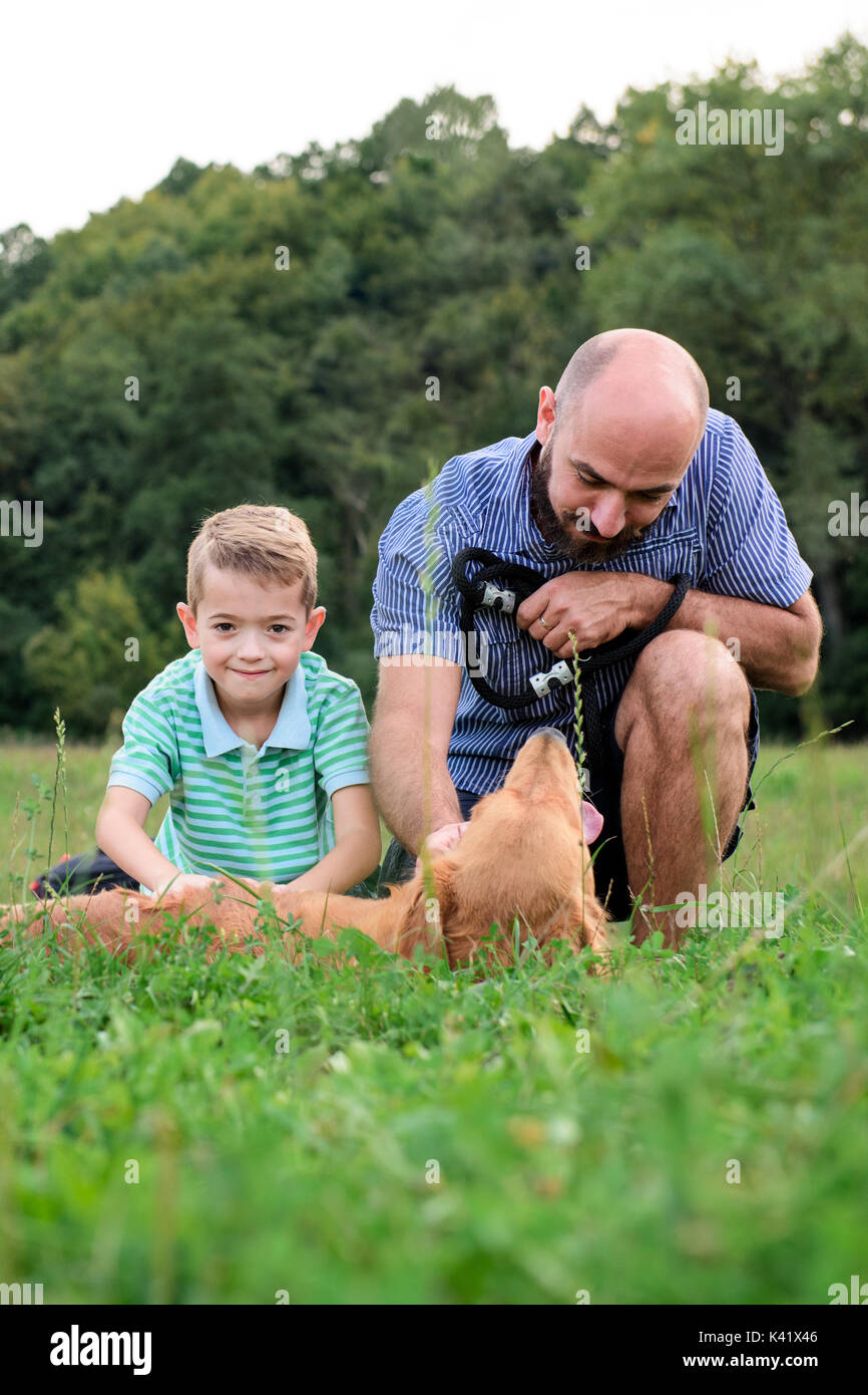 Adorabili e sorridente ragazzino con suo padre hipster, giocando con il proprio cane golden retriever Foto Stock