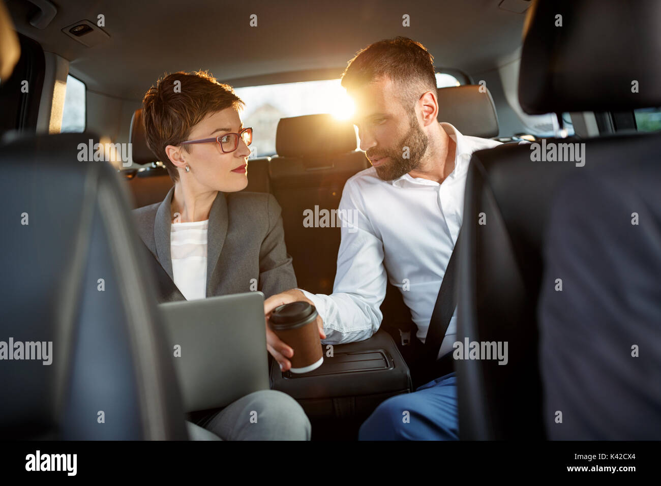 Imprenditore e imprenditrice utilizzando notebook per lavorare nel sedile posteriore della macchina Foto Stock