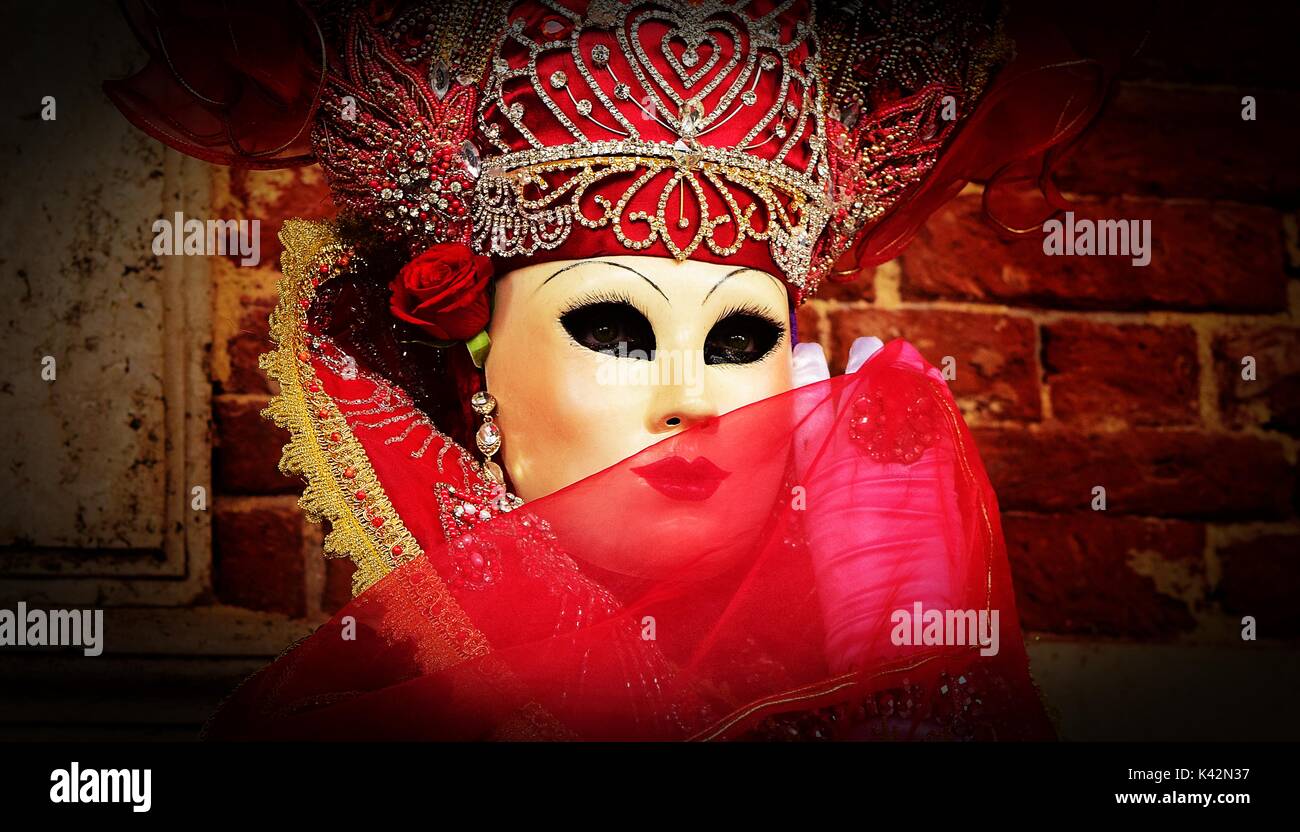 Una persona in un costume rosso durante un ballo in maschera presso il Carnevale di Venezia, coprendo la maschera con laccio rosso. Foto Stock
