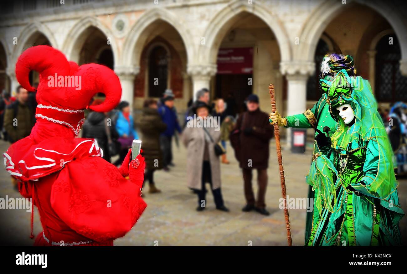 Una persona in rosso joker costume di carnevale di Venezia prende una foto di due altre mascherate in costume con il suo telefono cellulare. Foto Stock