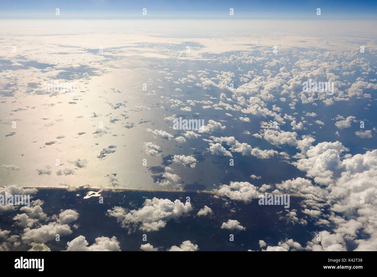 Vista aerea di mare e di terra da aereo visto dalla finestra, volare al di sopra delle nuvole. Foto Stock