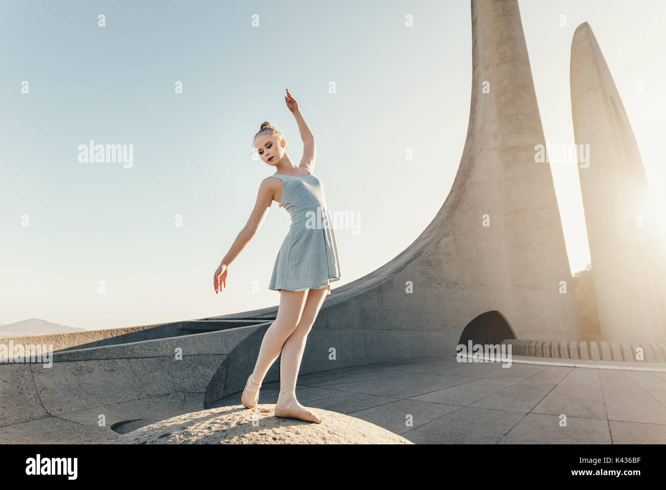 Ballet artista pratica di danza si sposta all'esterno. Ballerino femmina in piedi in un monumento la pratica di passi di danza con Sun in sfondo. Foto Stock