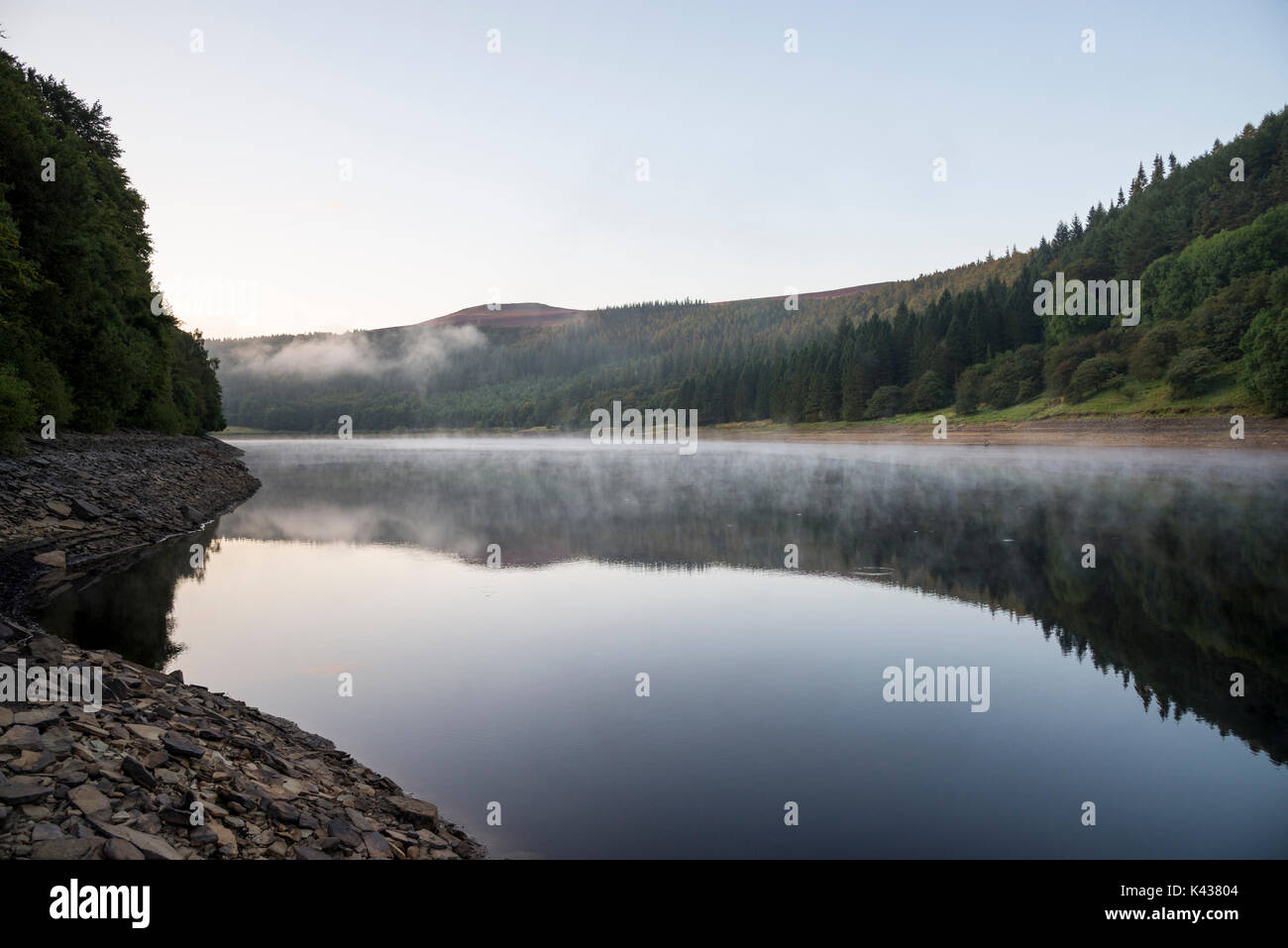 Incredibile settembre mattina al serbatoio Ladybower, Peak District, Derbyshire, in Inghilterra. Drifting di nebbia al di sopra della superficie dell'acqua. Foto Stock