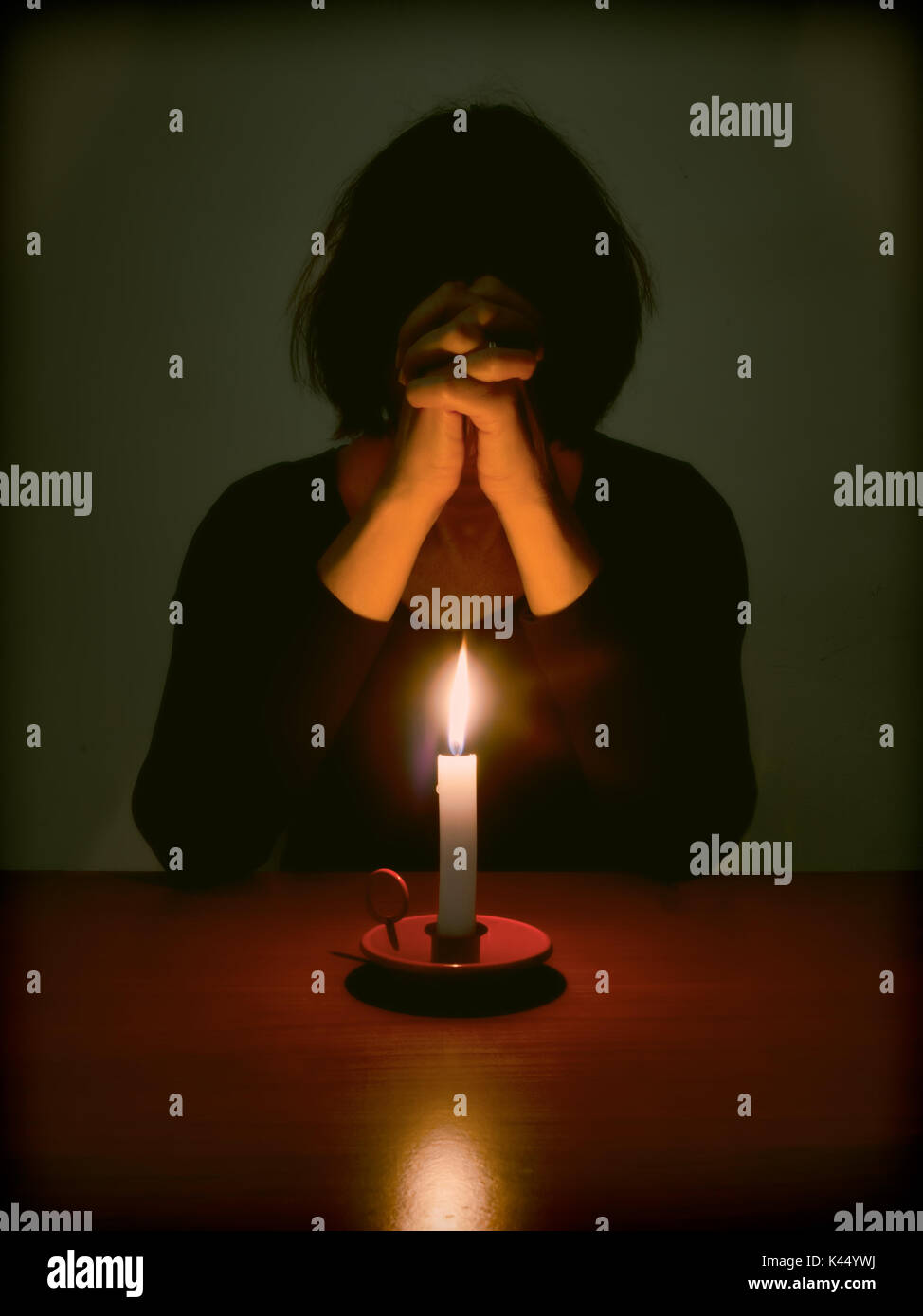 Immagine religiosa della donna in preghiera nella stanza buia a tavola. Foto Stock
