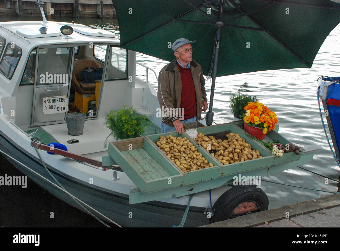 Uomo finlandese vendita di ortaggi da una barca nel porto di Helsinki, la città capitale della Finlandia Foto Stock