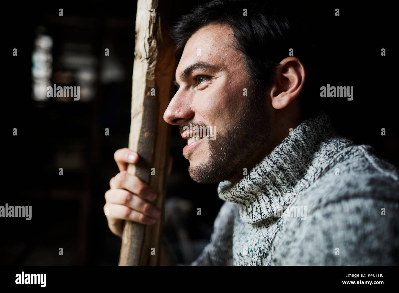 Granaio, uomo con maglia pullover e palo di legno, sorriso, ritratto, vista laterale Foto Stock