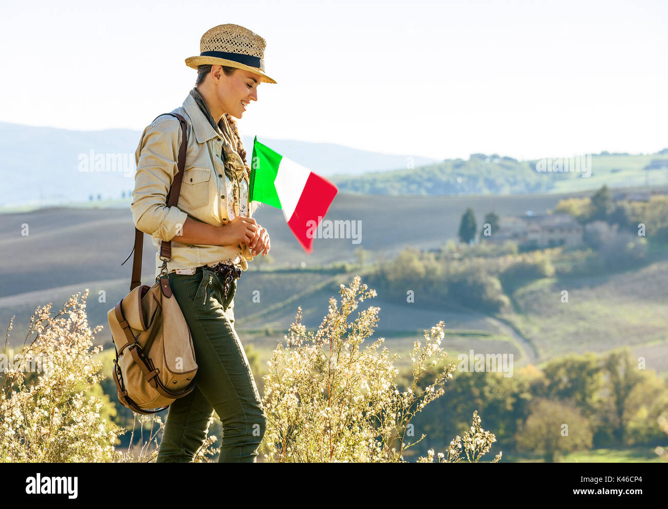 Alla scoperta di magiche vedute della Toscana. sorridente donna avventura escursionista in hat con bandiera italiana gode di vista in Toscana Foto Stock