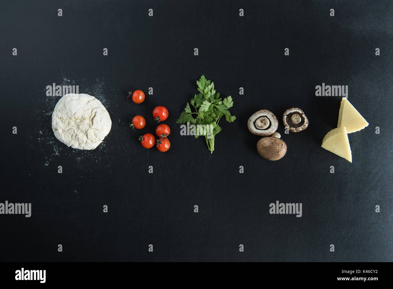 Vista superiore della pasta con gli ingredienti per la preparazione della pizza italiana sulla superficie scura Foto Stock