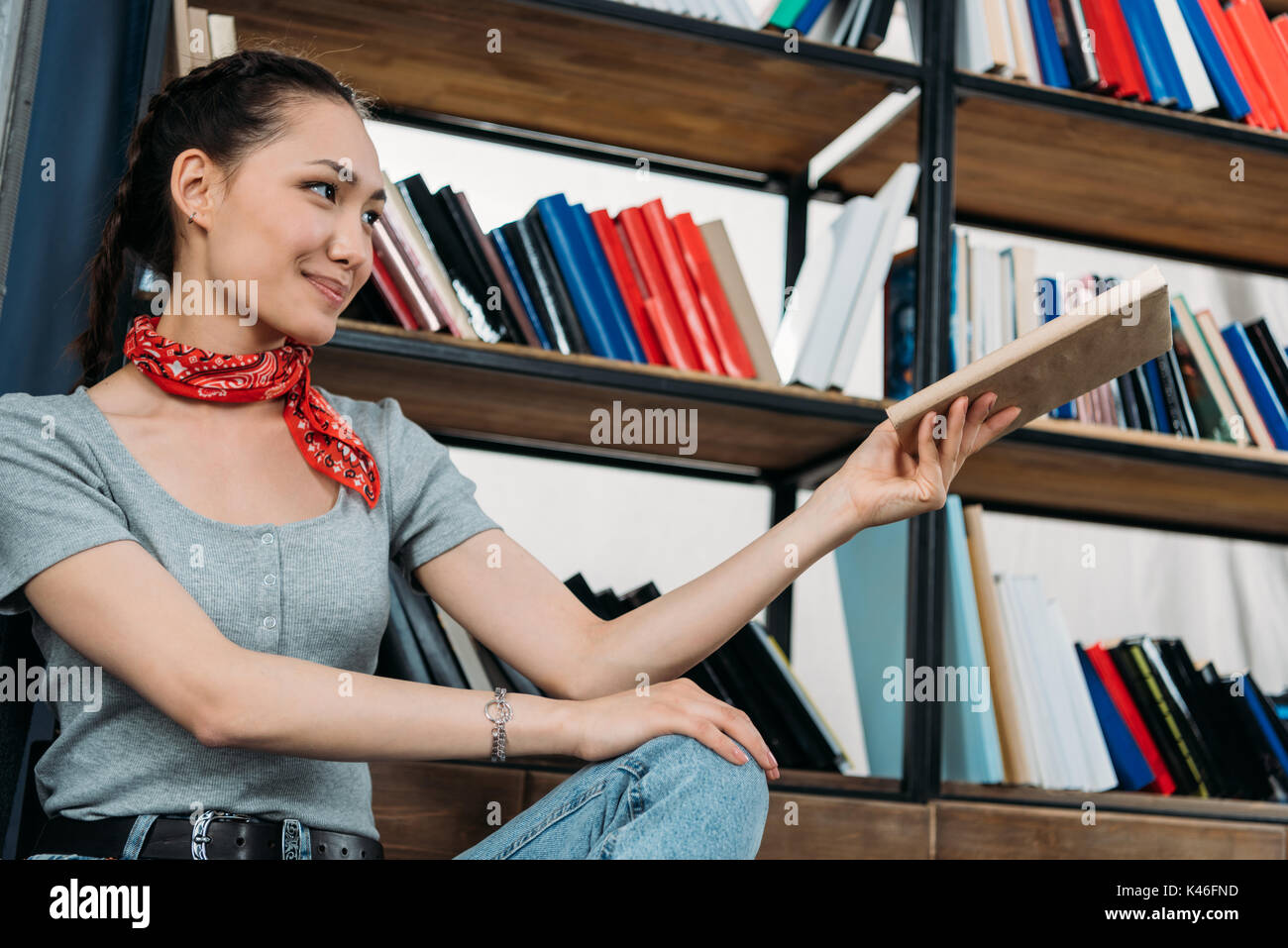 Giovane donna asiatica sorridente e azienda prenota at home biblioteca Foto Stock