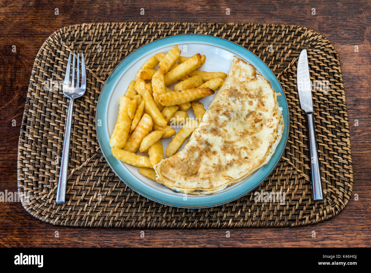 Essenziale ma gustoso pasto di frittata e crinkle Tagliare patate scheggiati, su Denby porcellanato piastra, con acciaio inox coltello e forchetta pronto all'uso. Foto Stock