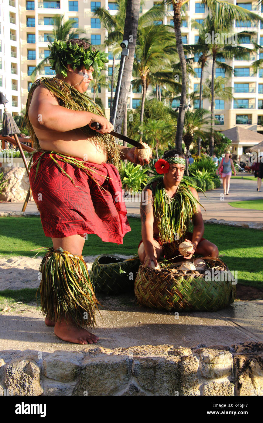 Luau Hawaiiano. Un uomo in un tradizionale costume hawaiano il taglio di un nuovo raccolto di noce di cocco. Ko Olina, Oahu, Hawaii. La foto è stata scattata in agosto 2015. Foto Stock
