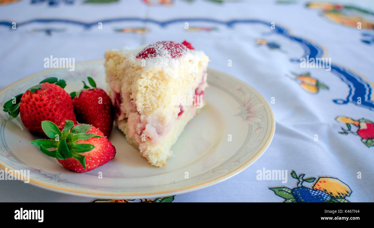 La torta di fragole e tre fragole con crema bianca sulla parte superiore, soft focus closeup, su bianco piastra di porcellana, sulla sommità di un panno blu sul tavolo da cucina Foto Stock