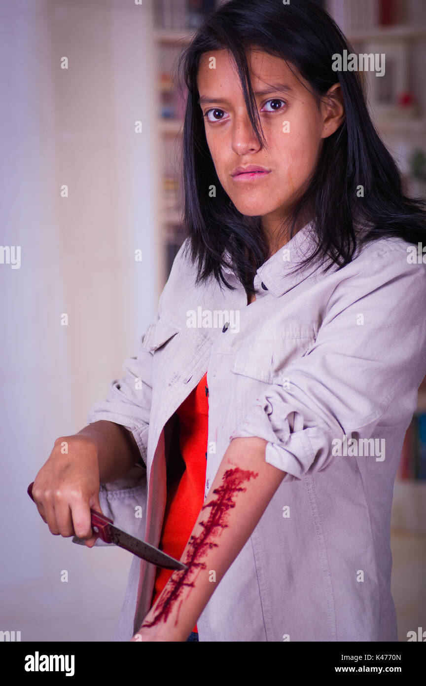Close up di un giovane adolescente depressivo tenendo un coltello con il suo braccio lo spurgo in uno sfondo sfocato Foto Stock