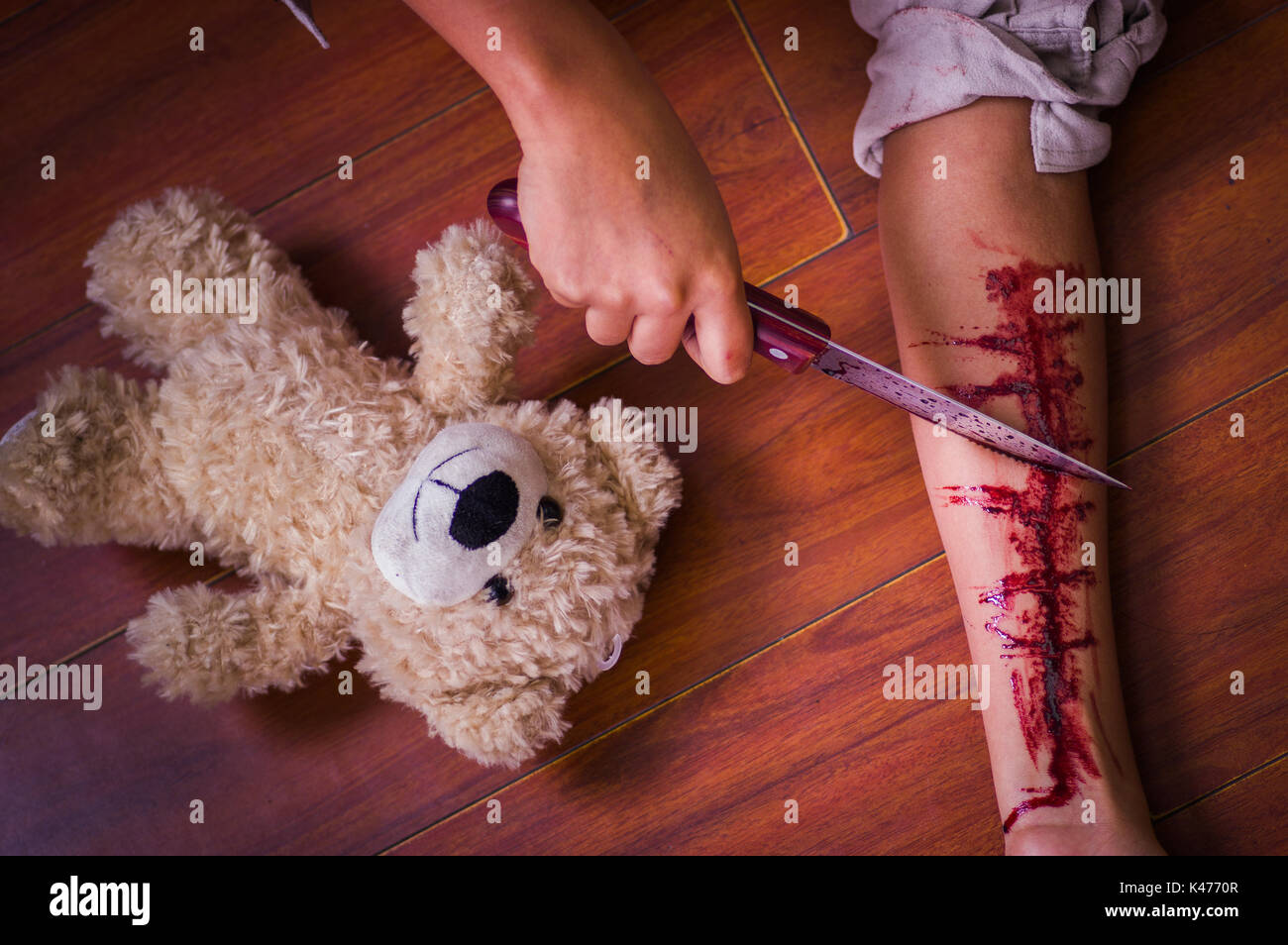 In prossimità di una giovane donna depressivo tenendo un coltello, con il suo braccio lo spurgo, con un orsacchiotto di peluche accanto a lei in uno sfondo di legno Foto Stock