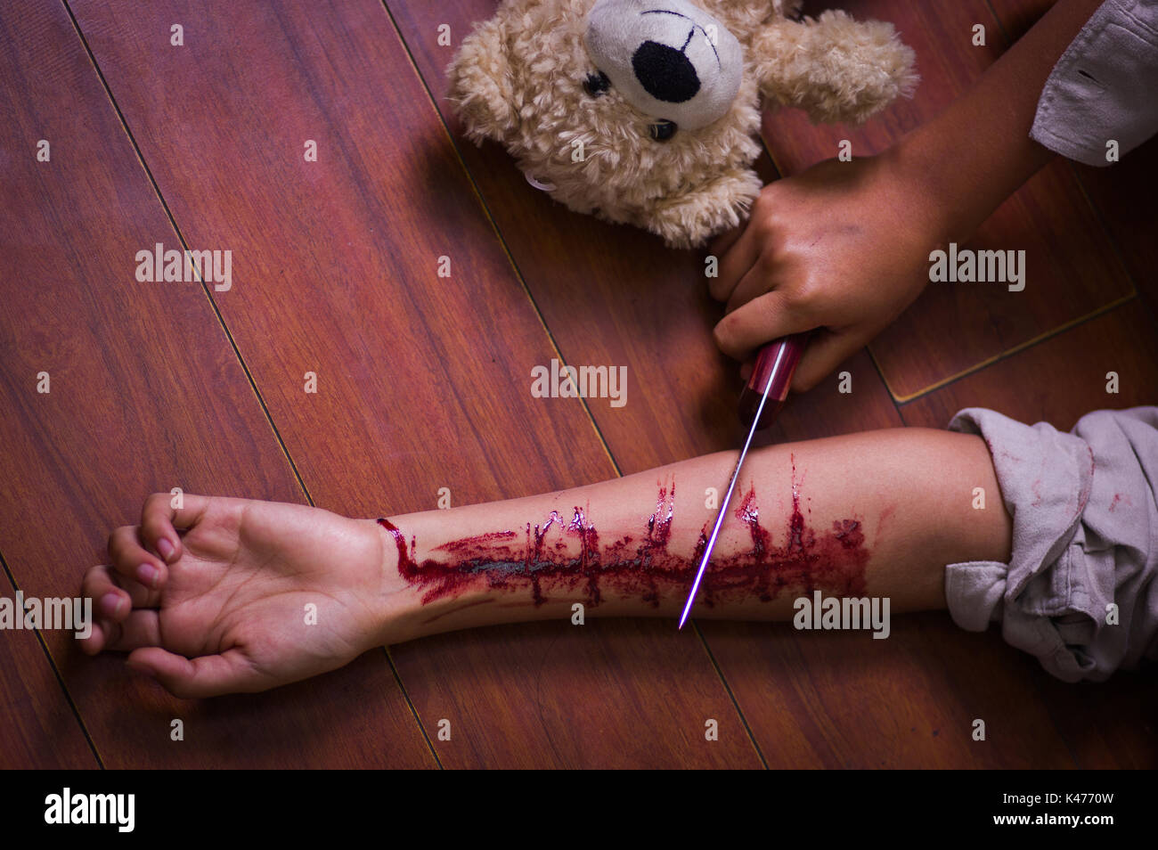 In prossimità di una giovane donna depressivo tenendo un coltello, con il suo braccio lo spurgo, con un orsacchiotto di peluche accanto a lei in uno sfondo di legno Foto Stock