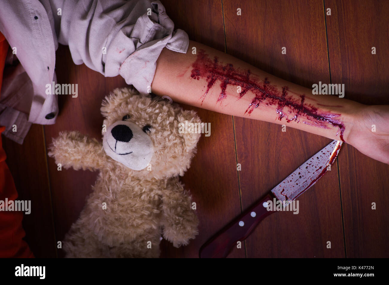 In prossimità di una giovane donna depressivo tenendo un coltello, con il suo braccio lo spurgo, con un orsacchiotto di peluche accanto a lei in uno sfondo di legno Foto Stock