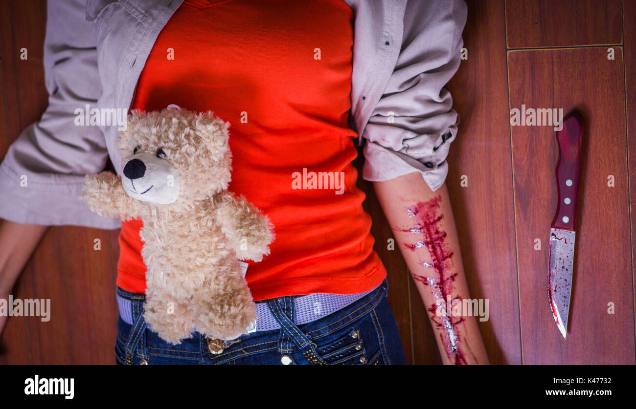 In prossimità di una giovane donna depressiva con il suo braccio lo spurgo con un orsetto nel suo ventre e un coltello accanto a lei in uno sfondo di legno Foto Stock