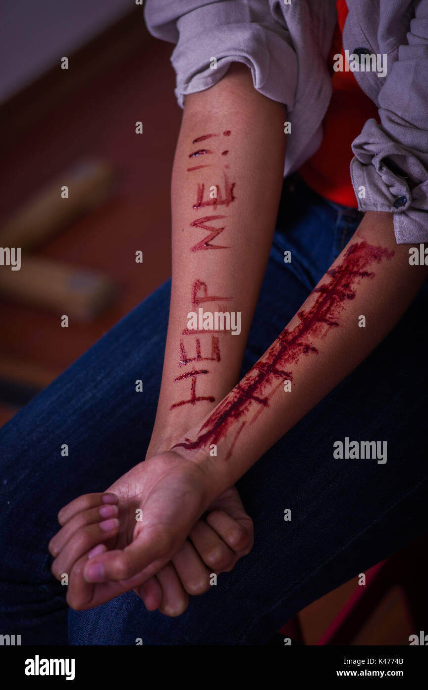 In prossimità di una giovane donna depressivo, con entrambe le braccia lo spurgo con la parola guida scritto nel suo braccio con un coltello, in uno sfondo sfocato Foto Stock