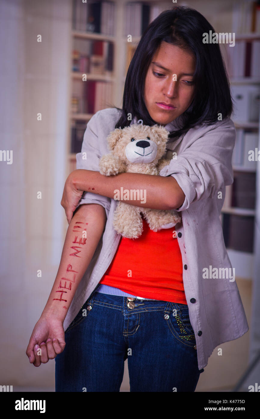 In prossimità di una giovane donna depressiva con il suo braccio lo spurgo, abbracciando un orso di peluche in uno sfondo sfocato Foto Stock