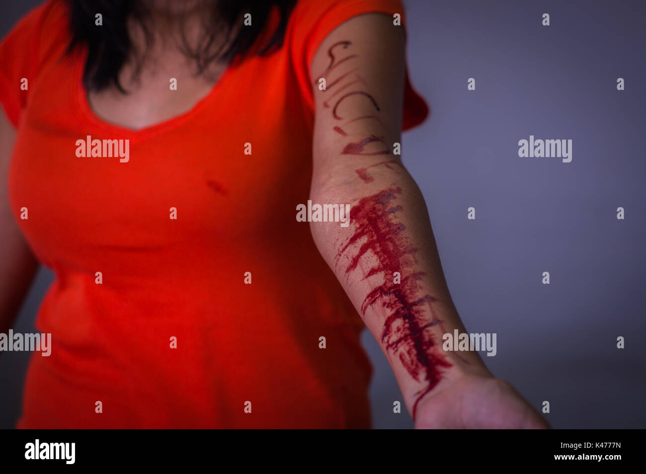 In prossimità di una giovane donna depressivo, con il suo braccio lo spurgo con la parola suicidio scritto nel suo braccio con un coltello, in uno sfondo sfocato Foto Stock