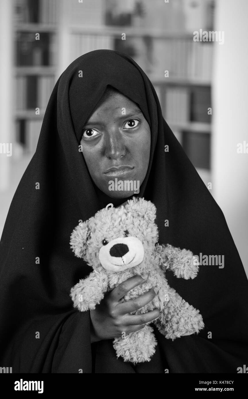 Ritratto di un triste ragazzina musulmana che indossa un hijab e tenendo le braccia il Teddy bear, in uno sfondo sfocato Foto Stock