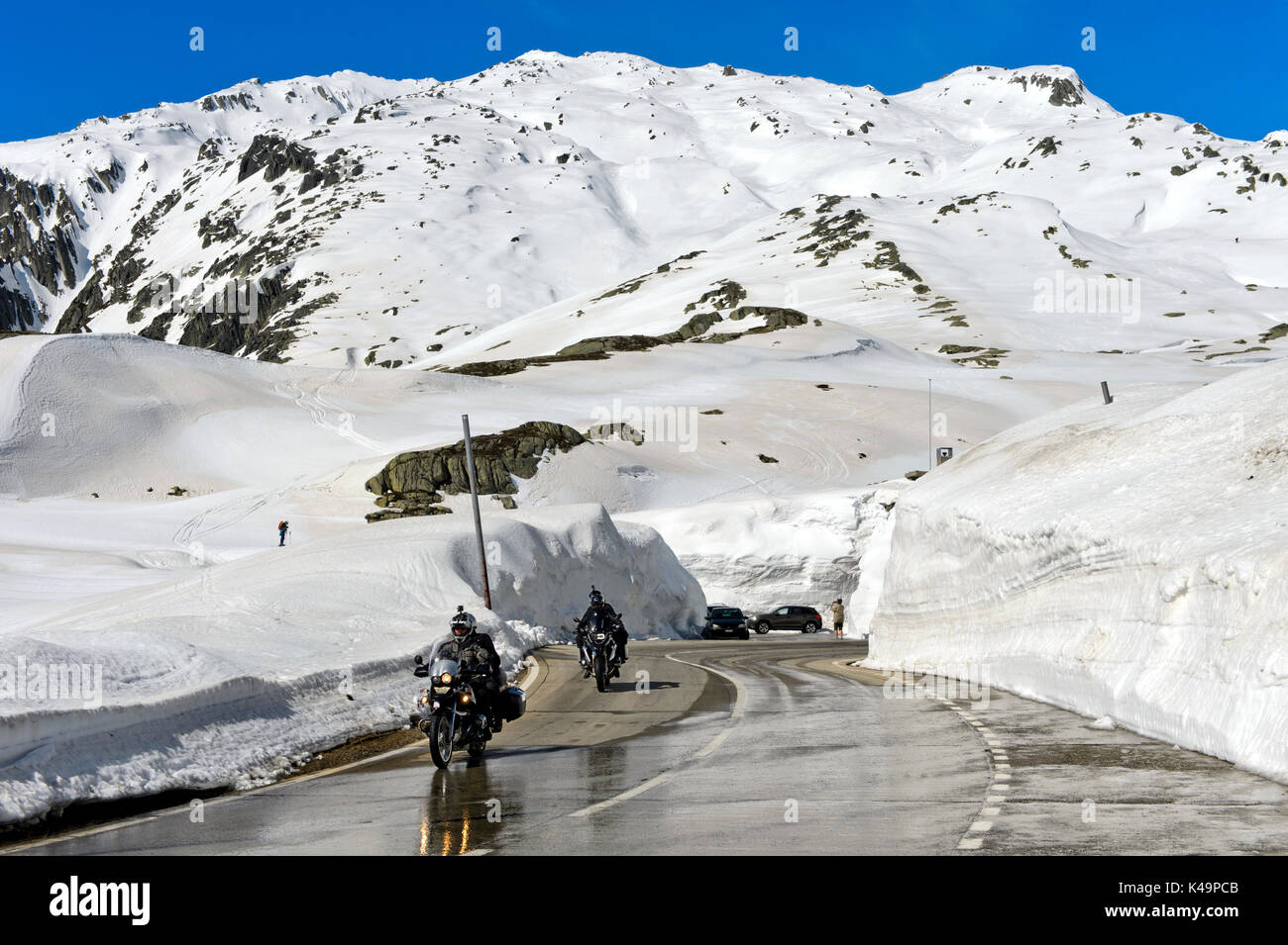 Due motociclisti che attraversa il San Gottardo sulla strada del passo tra muri di neve, Ticino, Svizzera Foto Stock