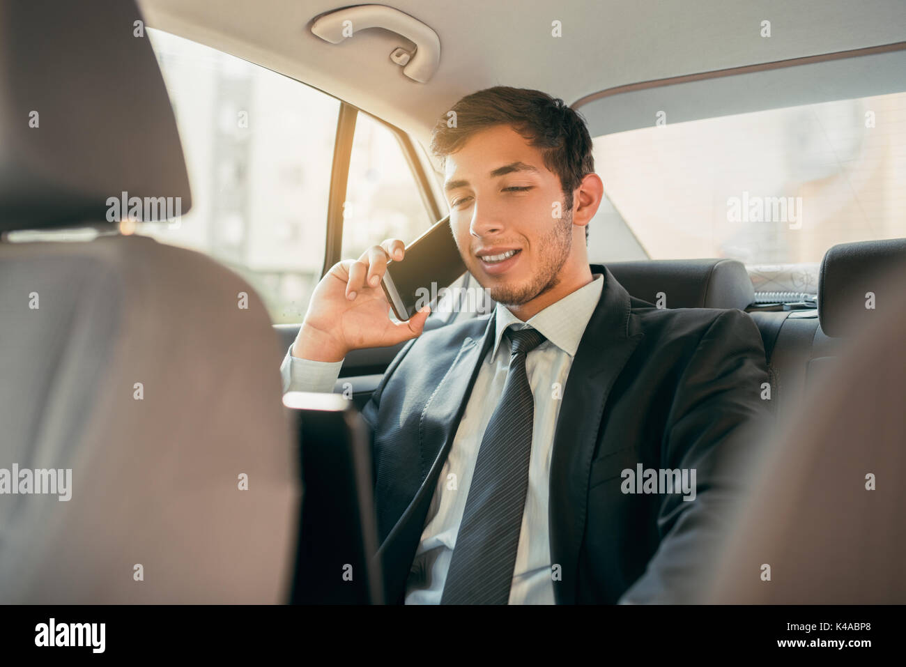 Imprenditore lavorare mentre è seduto in un'auto. L'uomo beeing pilotato a lavorare nel suo limo. Indossare giacca e cravatta imprenditore nel sedile posteriore facendo una chiamata mentre la limousine driver è la guida. Foto Stock