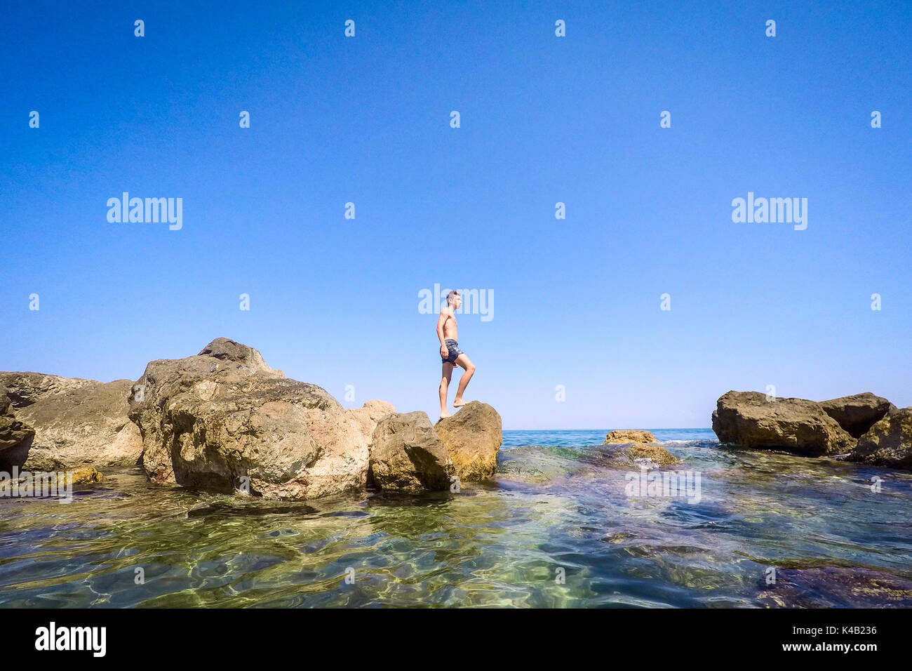 Adolescente in piedi sulle rocce al mare - estate - Sicilia mare mediterraneo Foto Stock