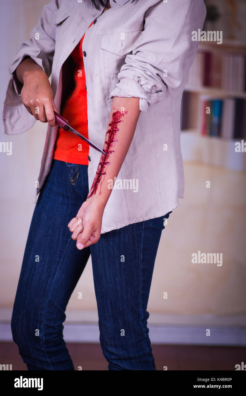 In prossimità di una giovane donna depressivo tenendo un coltello con il suo braccio lo spurgo in uno sfondo sfocato Foto Stock