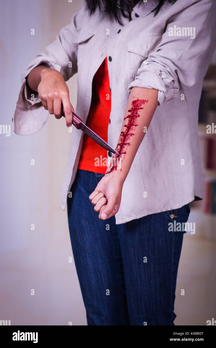 In prossimità di una giovane donna depressivo tenendo un coltello con il suo braccio lo spurgo in uno sfondo sfocato Foto Stock