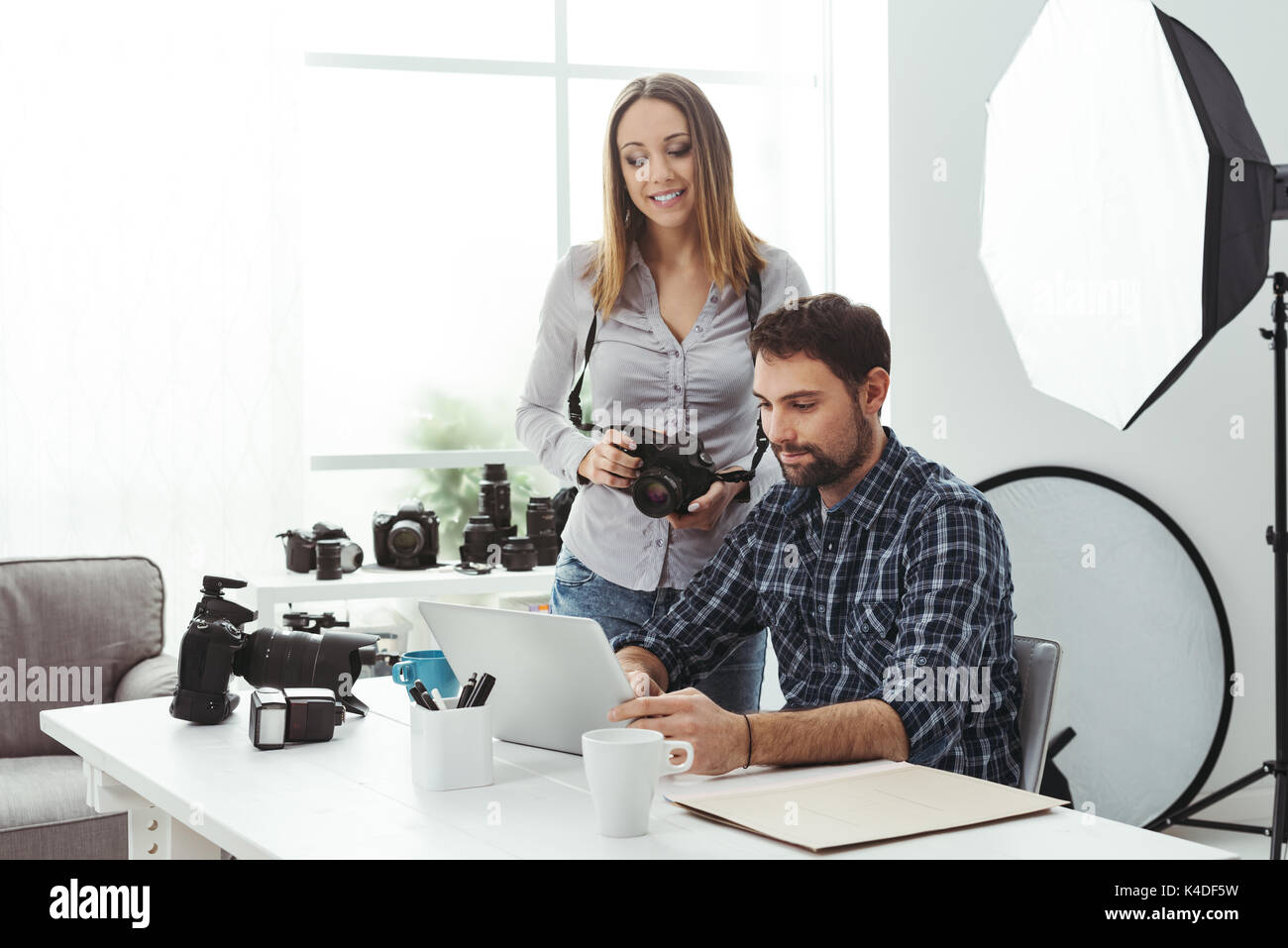 Fotografo e designer che lavorano insieme all'agenzia creativa, la donna è in possesso di una telecamera e l uomo è il collegamento con un computer portatile Foto Stock