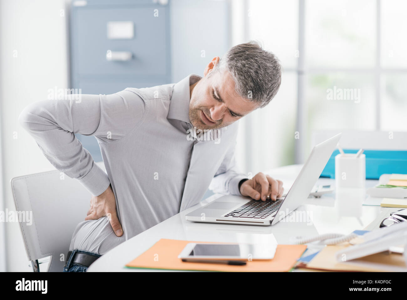 Sottolineato imprenditore con un mal di schiena, egli sta lavorando presso l'ufficio di accoglienza e del massaggio schiena Foto Stock