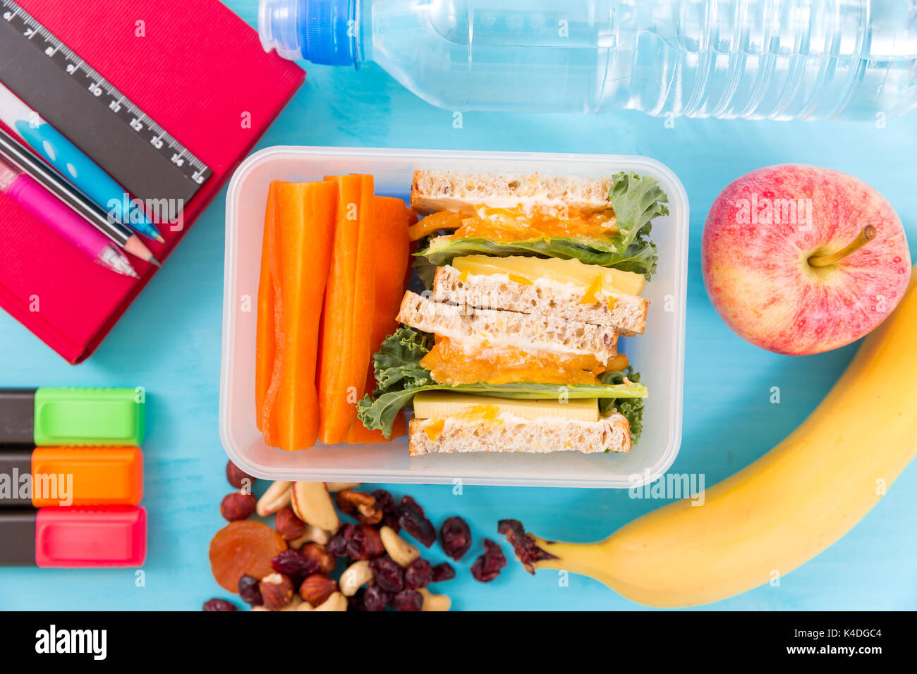 Scuola scatola di pranzo con sandwich, verdure, acqua, dadi e frutti su sfondo turchese. Abitudini alimentari sane concept Foto Stock