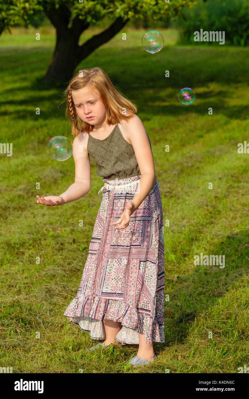 Ragazza giovane concentrando sulla cattura di una bolla di sapone al di fuori Foto Stock